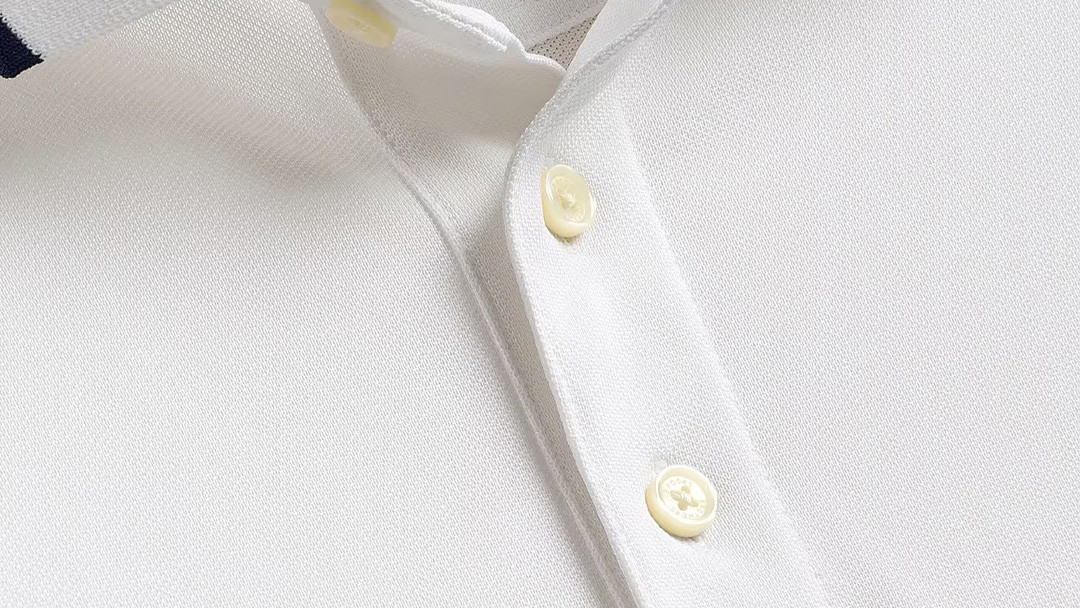 Close-up of a white golf polo shirt showing a flat fused placket and cross-stitched buttons