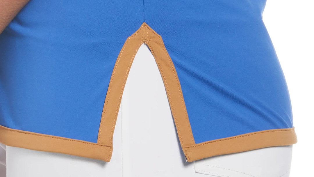 Detail of a blue performance polo hem showing a side vent reinforced with woven binding tape