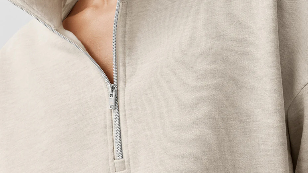 Close-up of a light beige textured knit quarter-zip pullover showing a flat fused placket and collar construction.