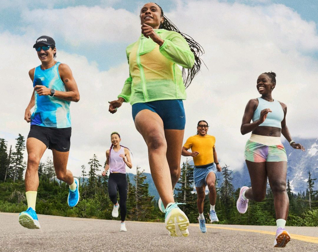 A diverse group of five people running on a scenic mountain road wearing brightly colored functional activewear.