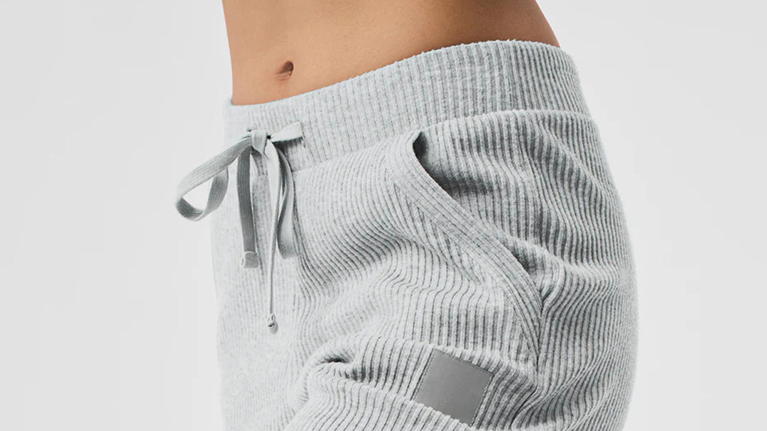 Detail of a wide, low-tension multi-needle stitched waistband and soft drawstring on ribbed loungewear pants.