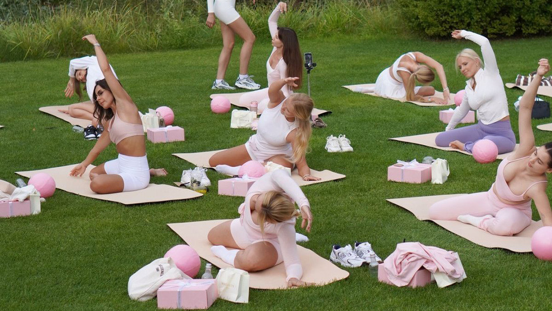 Container ships at a port, representing global trade and tariffs Group of women doing outdoor yoga wearing light pink and white custom activewear sets on mats.