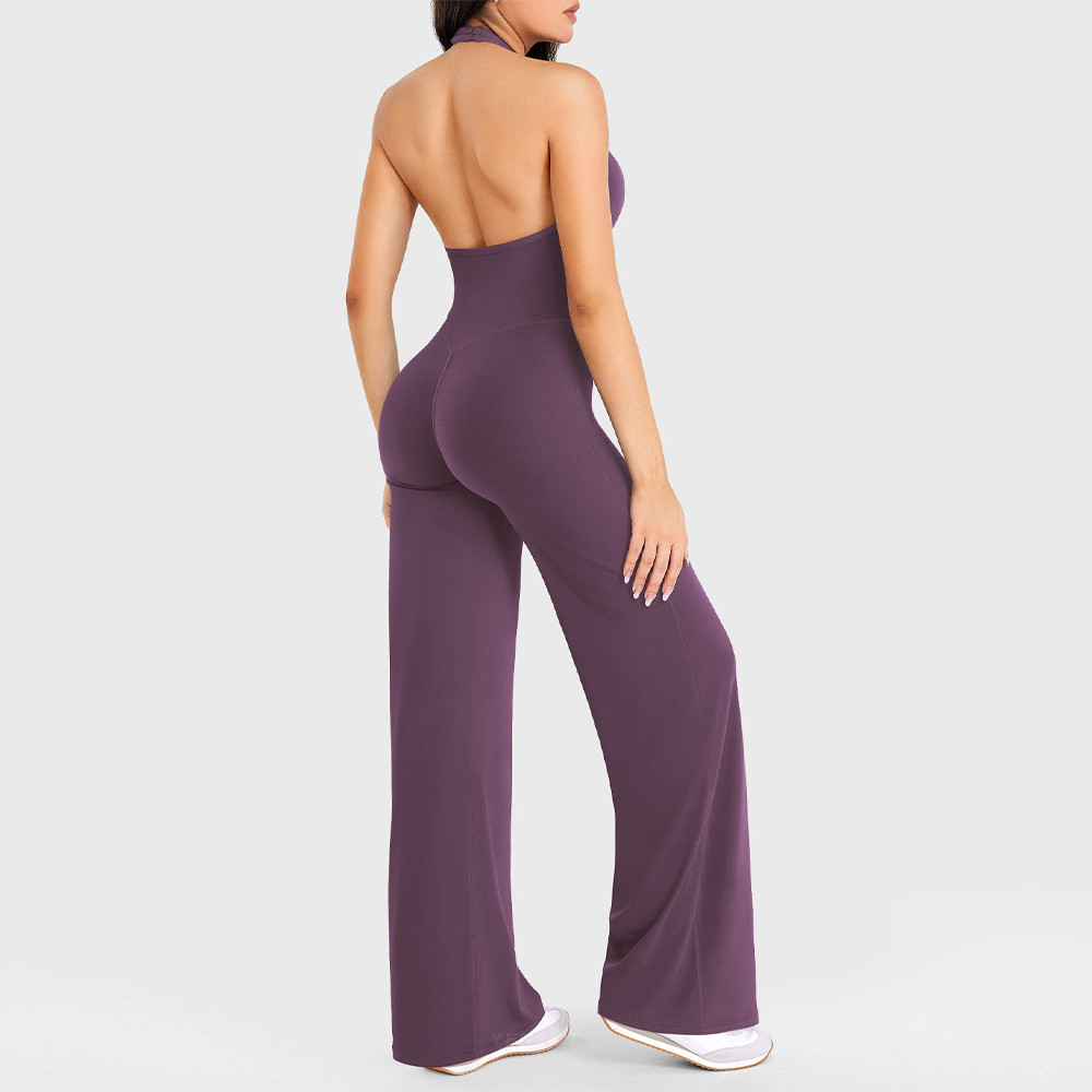 Rear full body view of purple yoga jumpsuit showing open back halter construction rear contour seams and wide straight leg openings