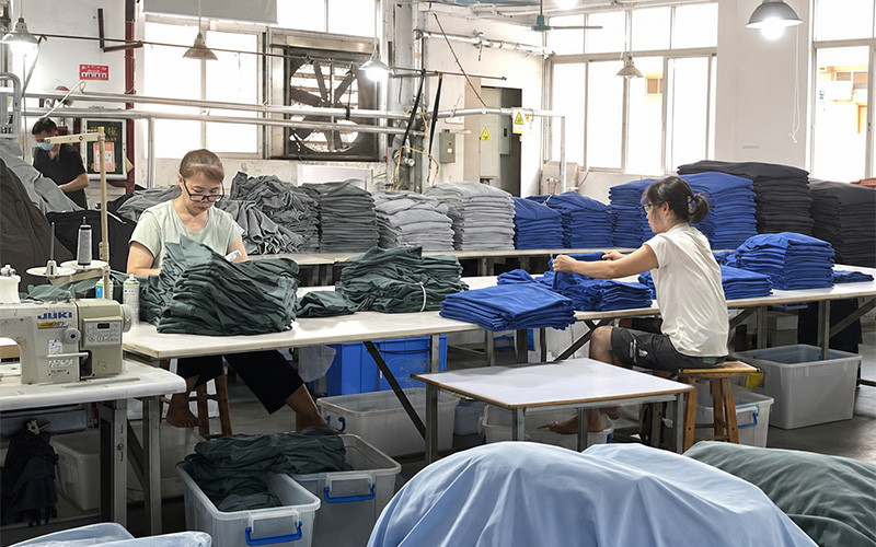 Workers folding garments beside stacks of clothing in a production workshop