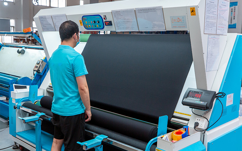 Worker inspecting dark fabric on a fabric inspection machine