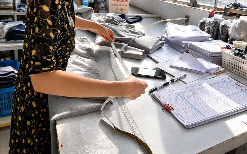 Worker measuring a gray garment beside a production worksheet