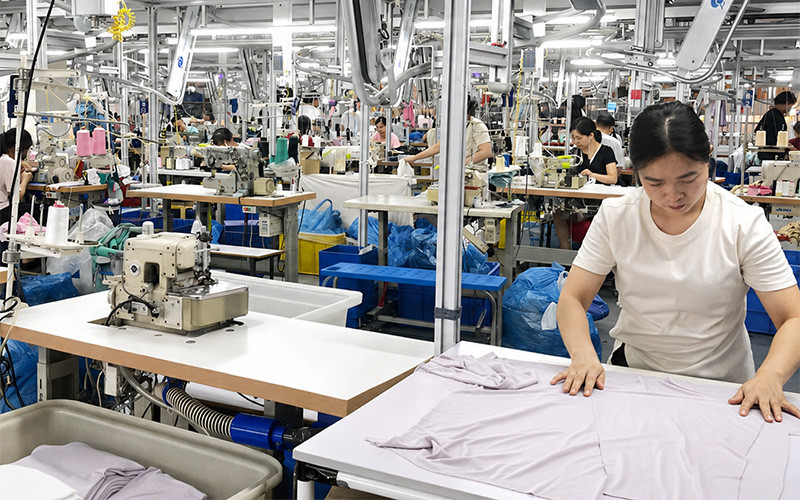 Worker laying out a light-colored garment beside a sewing machine