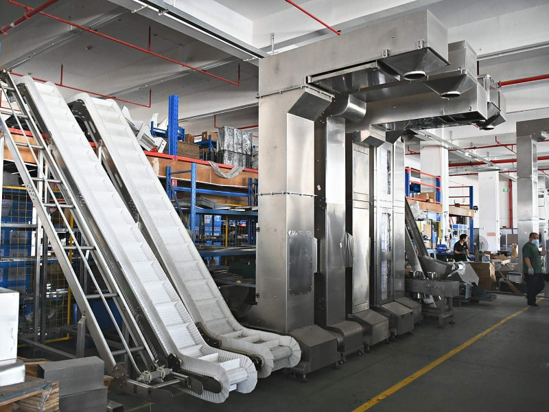 Workers assembling packaging machinery beside belt conveyors