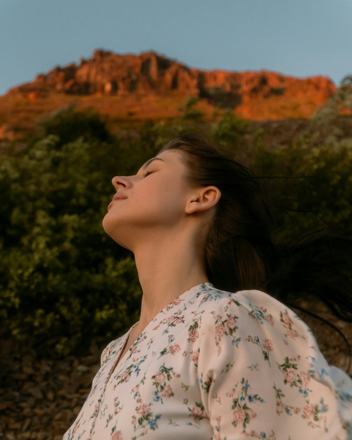 Woman sitting on a cliff overlooking mountains, breathing in fresh mountain air