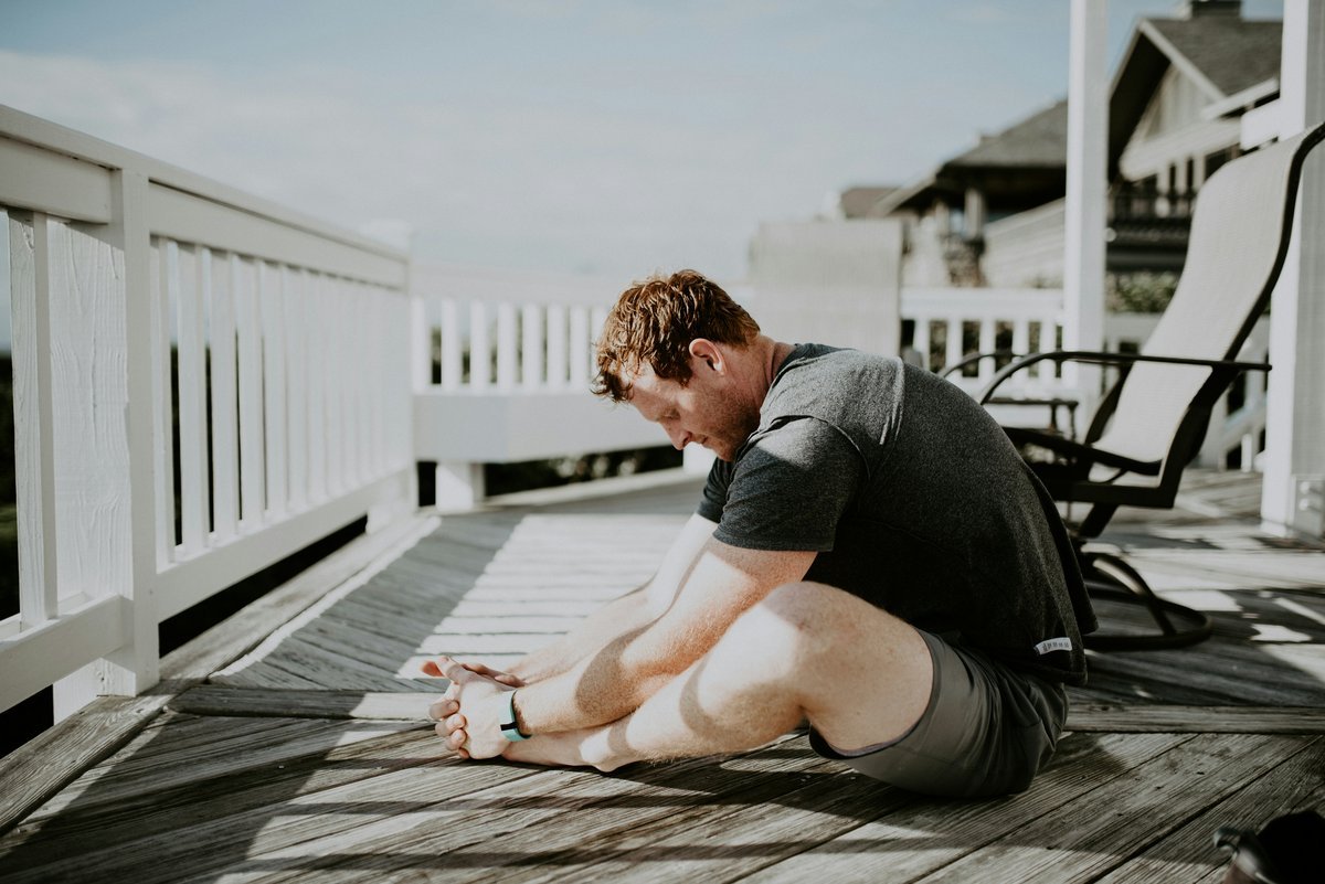 Man doing yoga and stretching on a porch with morning sunlight