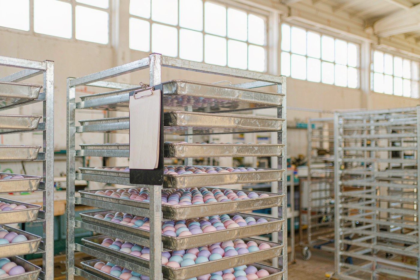 Steel curing racks holding trays of pastel squishy balls with a batch clipboard