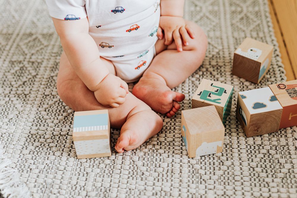 A baby sitting on a rug playing with wooden blocks