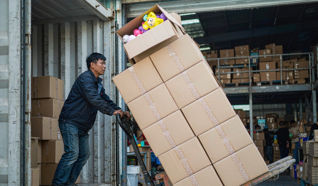 A worker moving cartons of squishy toys toward a shipping container at a Yiwu warehouse