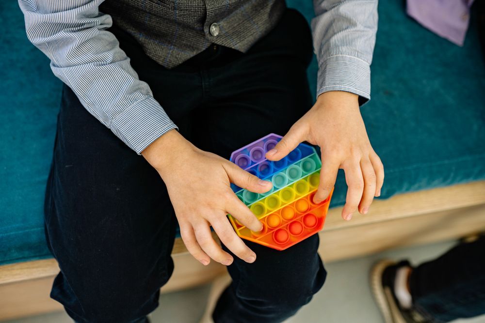 A pair of hands squeezing a rainbow marbled pop-it cube