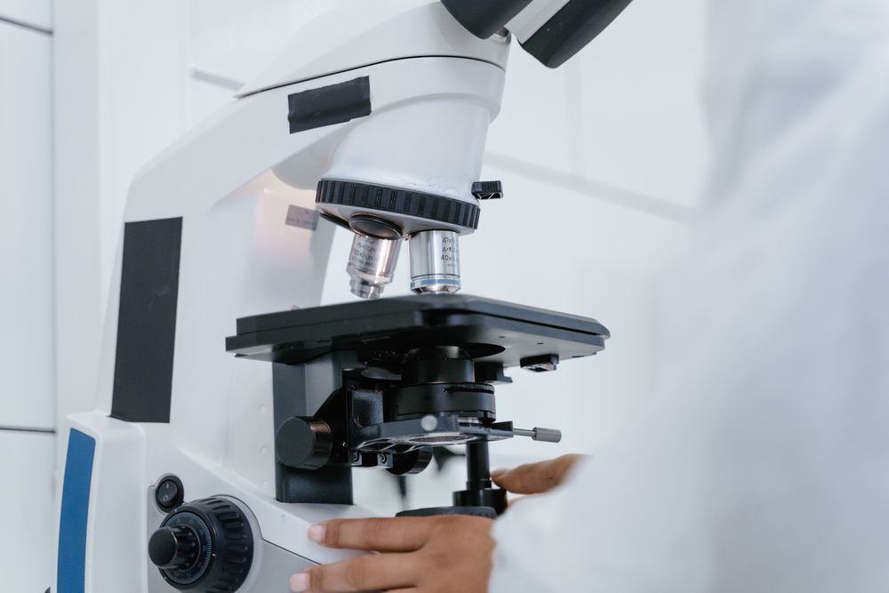 A laboratory microscope being used by a gloved technician