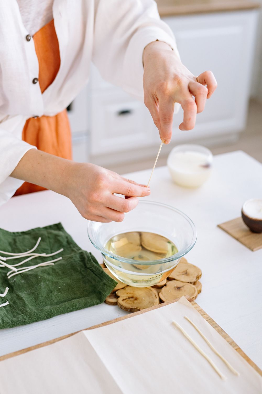 A person setting a wick while crafting wax, with melted wax and wicks laid out