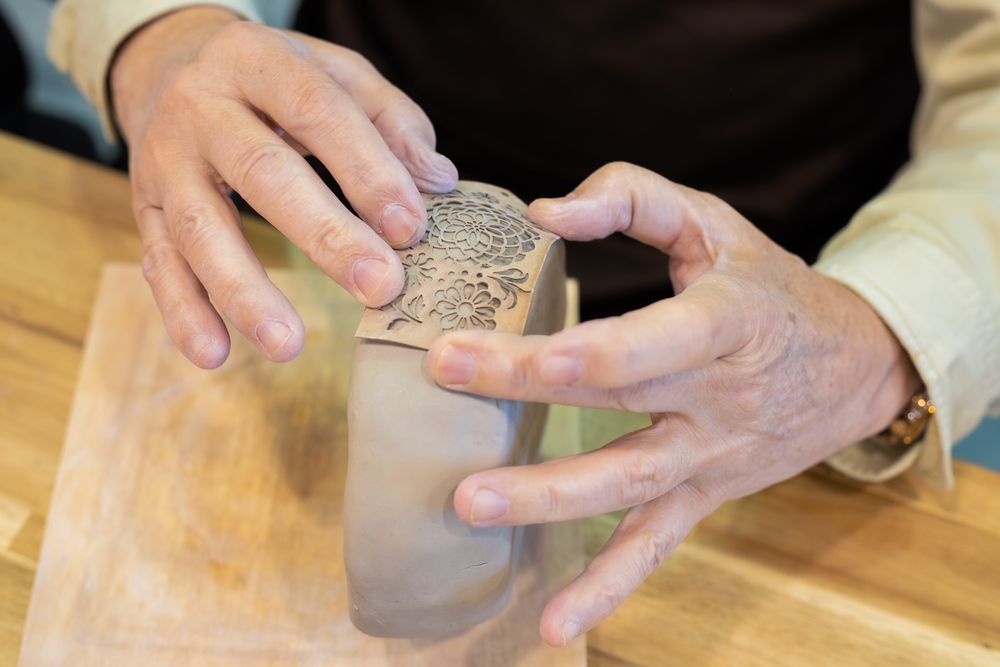 Two hands pressing and shaping a soft clay form on a wooden surface