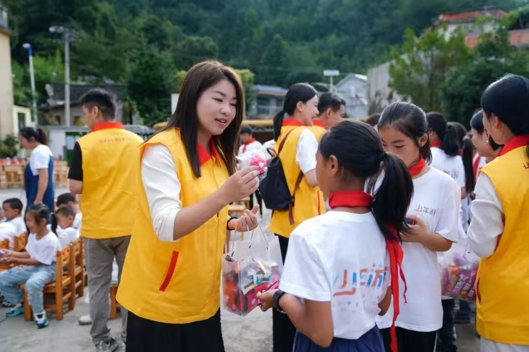 easemotion female volunteer interacting with young students, distributing care packages during the Baigu primary school charity activity