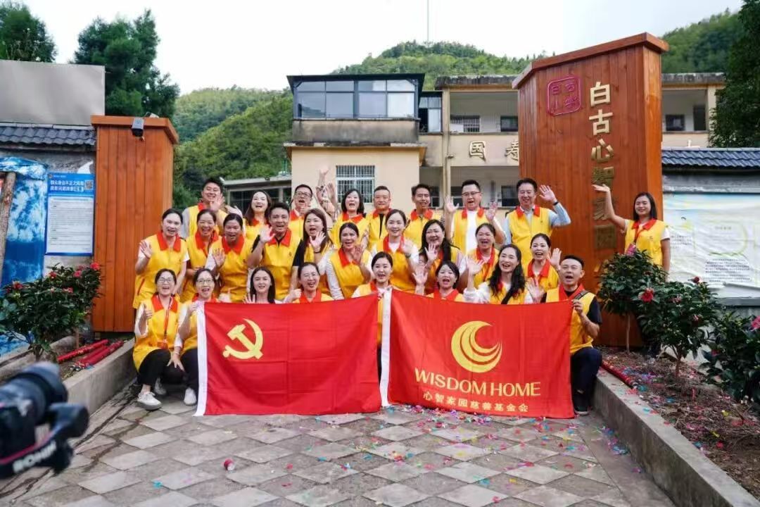 Group photo of easemotion volunteers with the Communist Party of China flag and Wisdom Home Foundation banner at the Baigu school charity launch