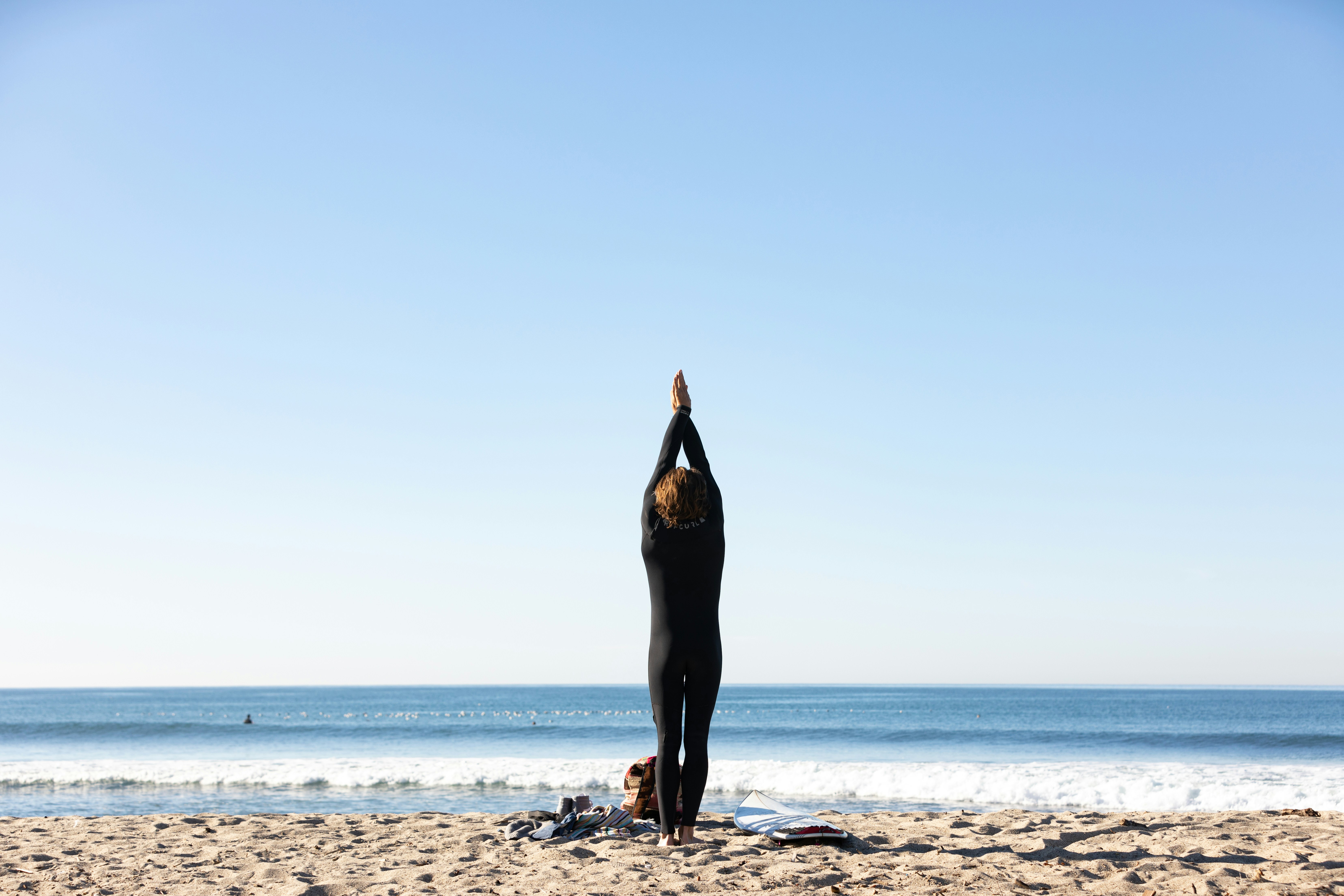 A person practicing yoga on a sunny beach, wearing a long-sleeved UPF-rated top and leggings.