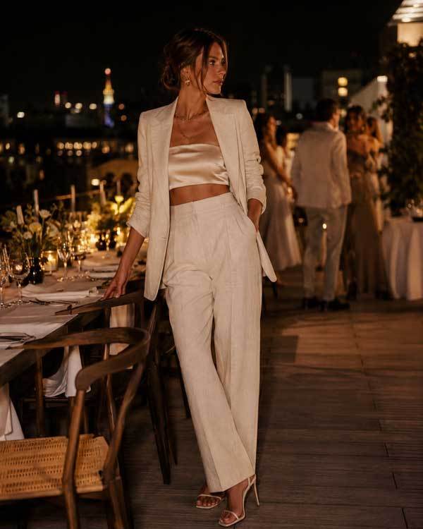 A woman wearing a relaxed linen button-up shirt with rolled sleeves, paired with denim shorts and leather sandals, standing in a sunlit garden or outdoor café, casual lifestyle fashion photography, warm natural lighting.