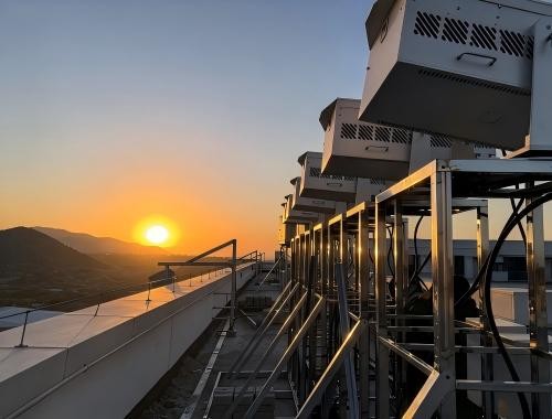Weather-exposed outdoor laser lights mounted on truss frames in a rooftop installation at sunset, silhouetted against mountains