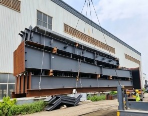 The steel structure is being crane‑lifted onto the trailer.