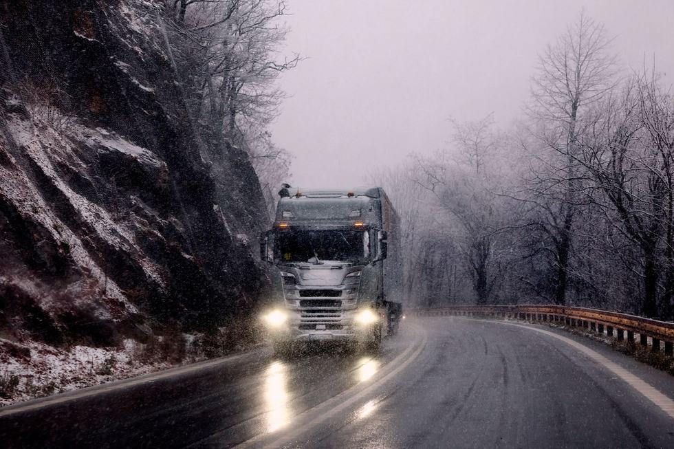 Articulated truck driving through snow on a mountain road in winter