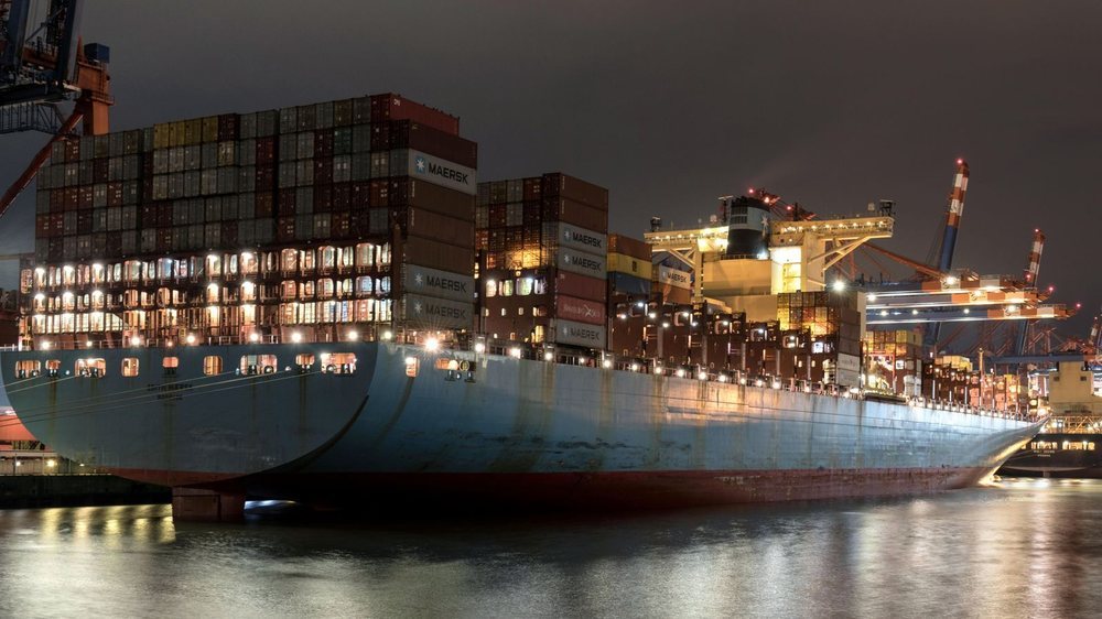 Container ship alongside a harbour berth at dusk with stacked containers on deck