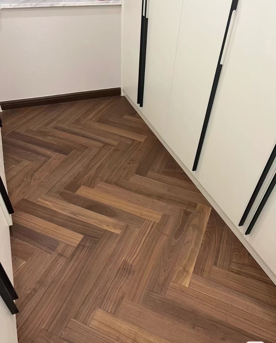 Close-up detail of oak 3-layer herringbone engineered wood flooring in a warm walnut tone, showcasing smooth UV lacquer surface, precise craftsmanship, natural wood texture, and rich mid-century character.