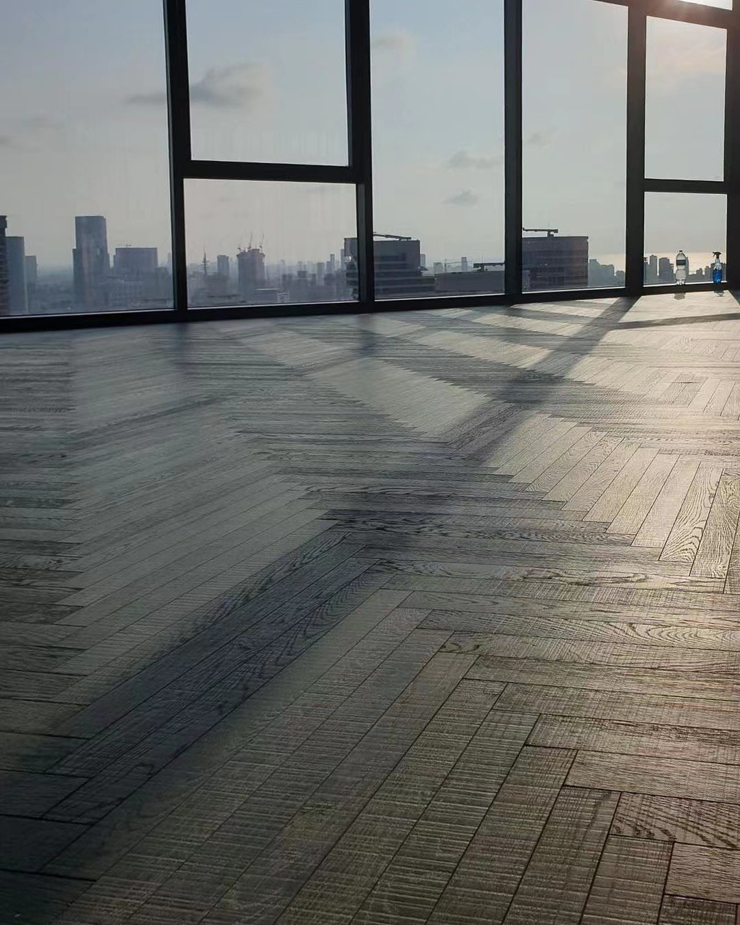 Dark wide herringbone engineered oak flooring installed in a modern luxury penthouse in Dubai with panoramic skyline views and minimalist interior styling.