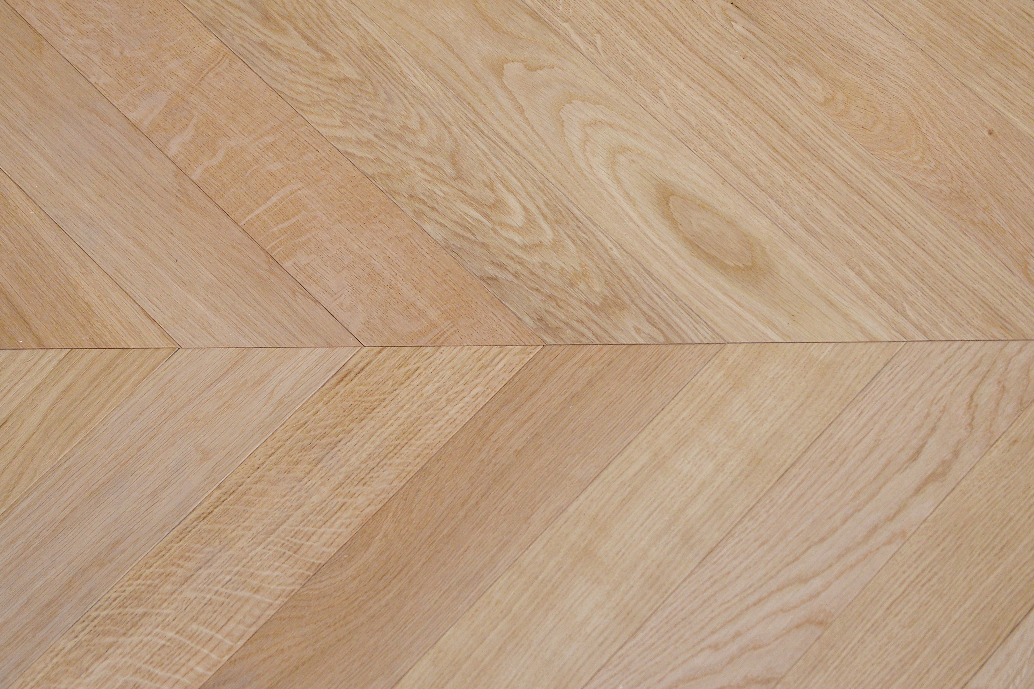 Precise chevron joint detail of three-layer engineered warm natural oak flooring, clean V-pattern parquet installation with organic grain texture