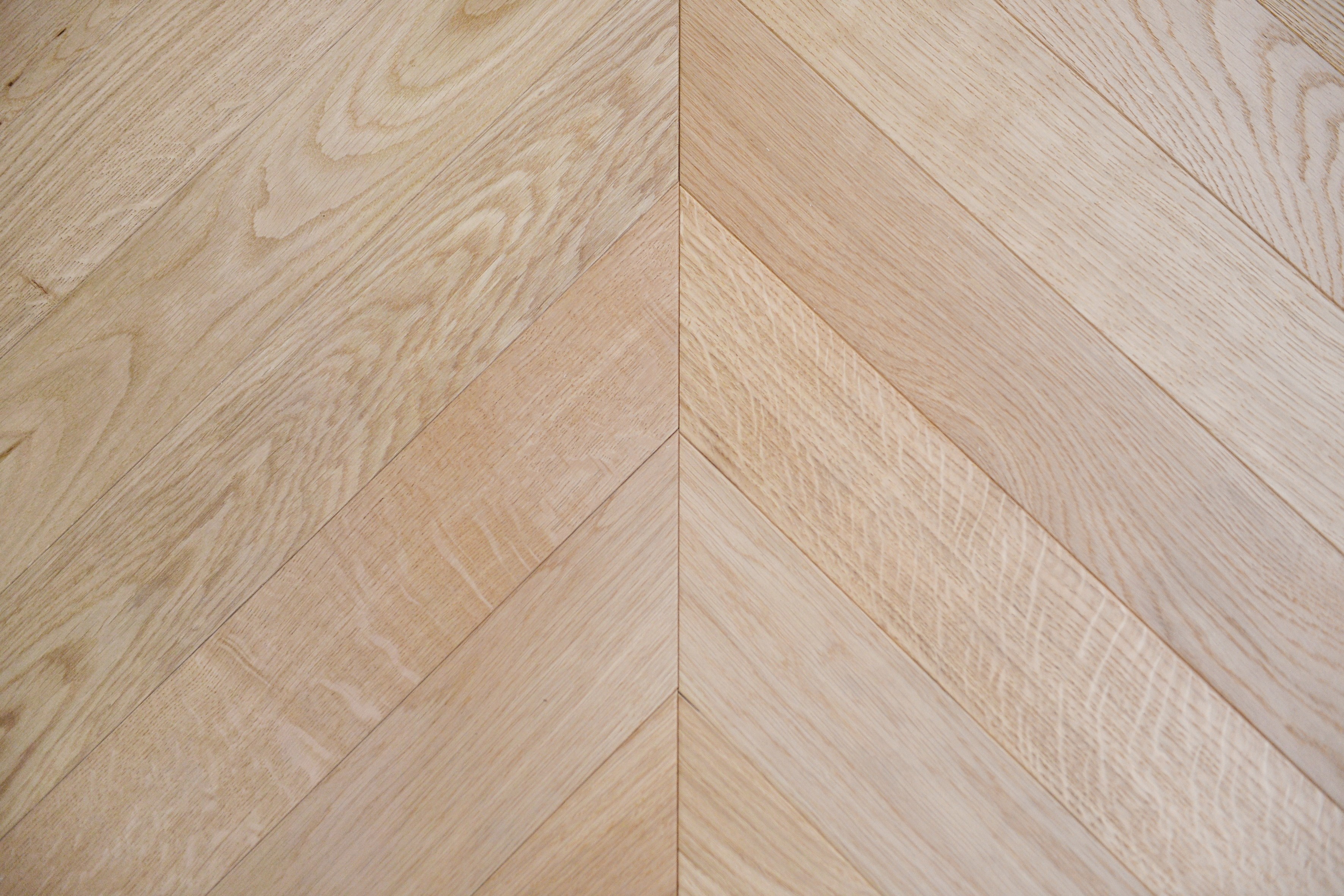 Precise chevron joint detail of three-layer engineered warm natural oak flooring, clean V-pattern parquet installation with organic grain texture