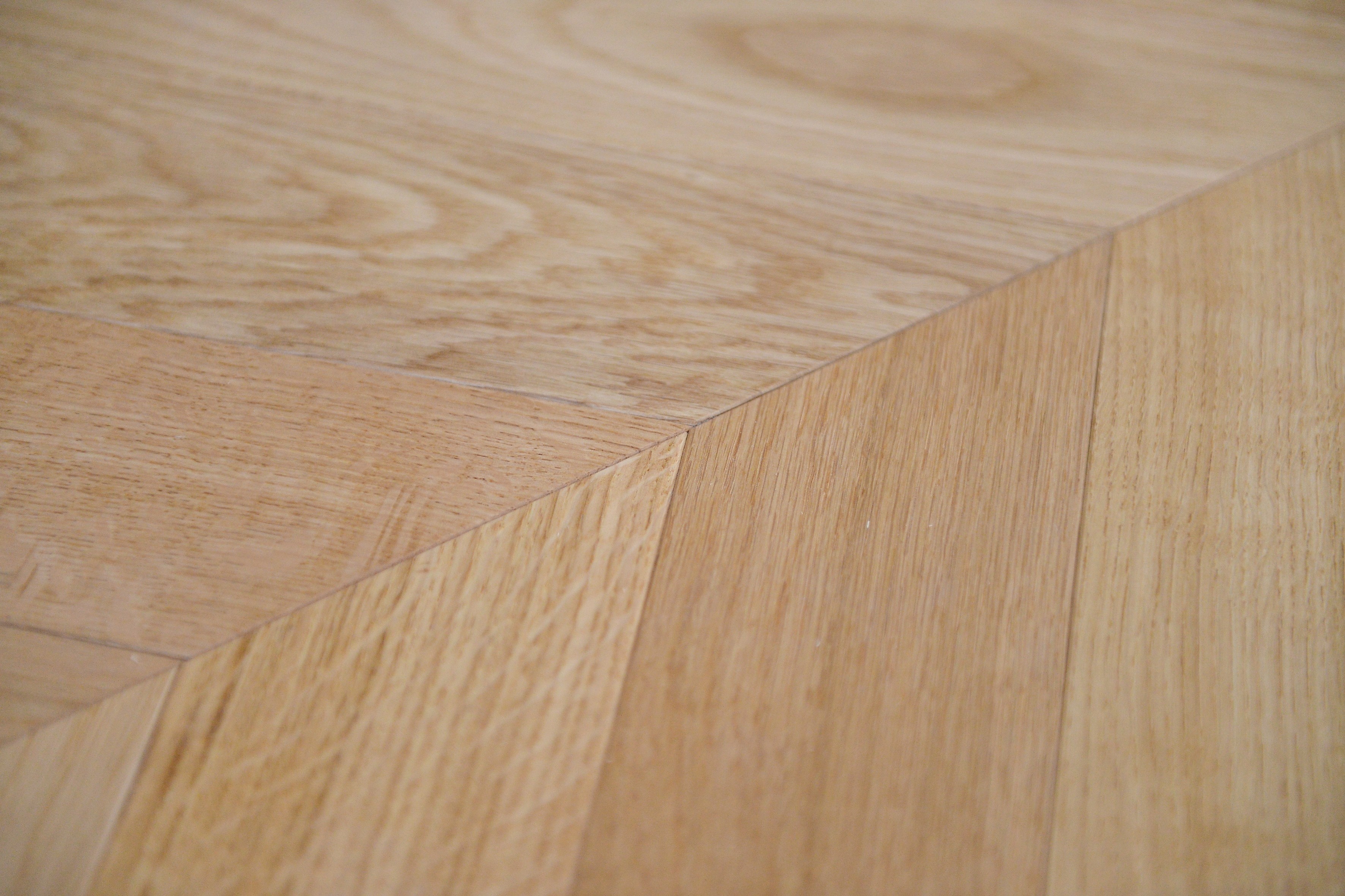 Precise chevron joint detail of three-layer engineered warm natural oak flooring, clean V-pattern parquet installation with organic grain texture