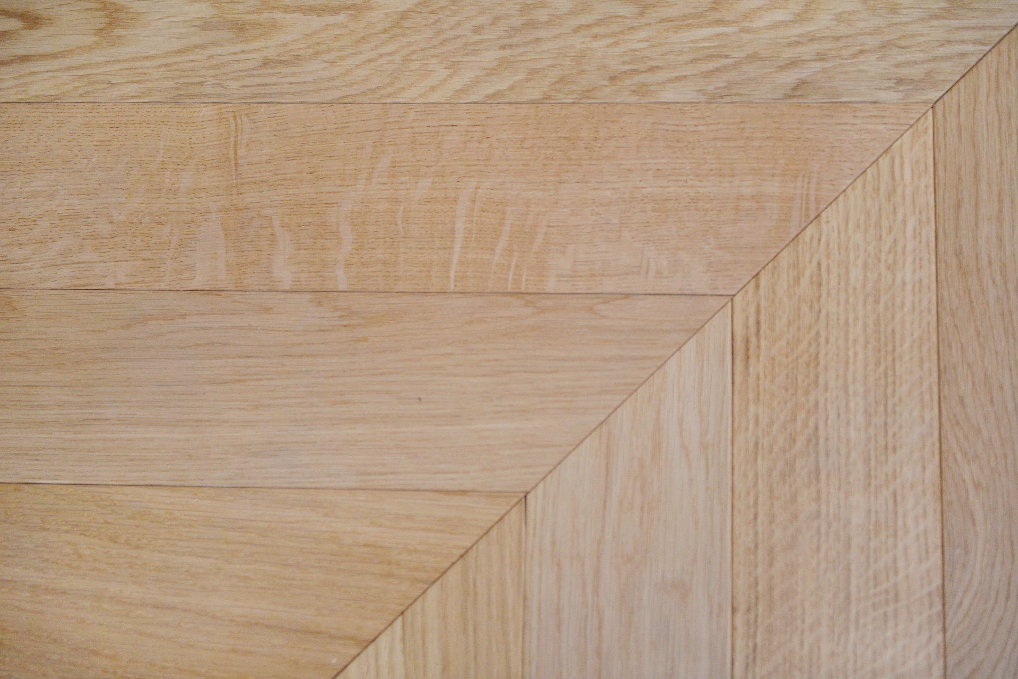 Precise chevron joint detail of three-layer engineered warm natural oak flooring, clean V-pattern parquet installation with organic grain texture
