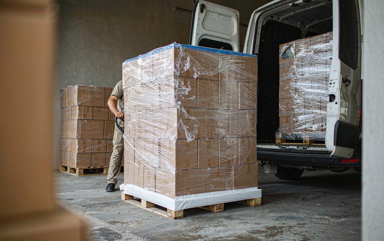 Pallet of shrink-wrapped cartons being moved into a delivery van at a loading bay