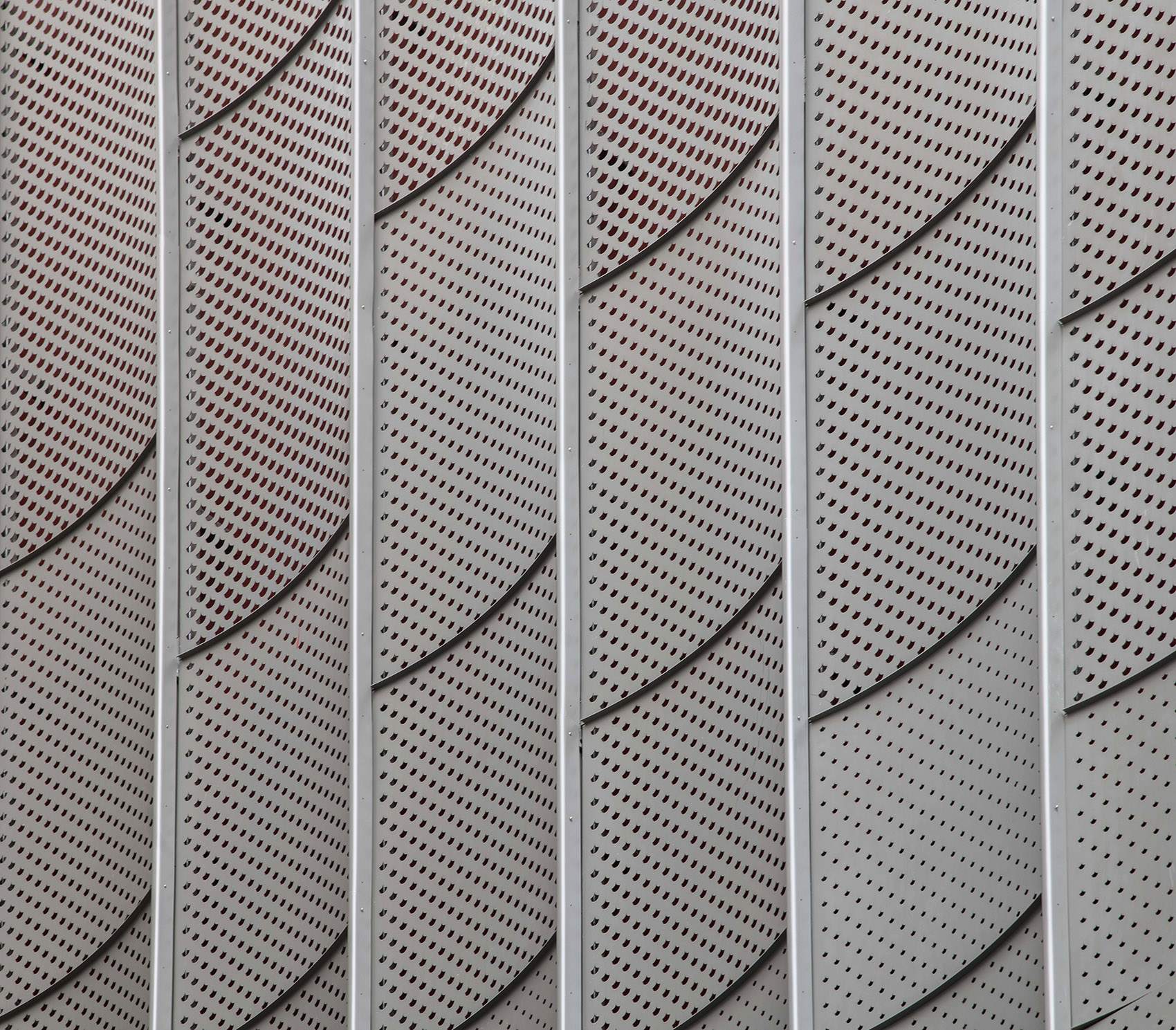 Perforated stainless steel facade panels forming a curved arc pattern on a cultural building