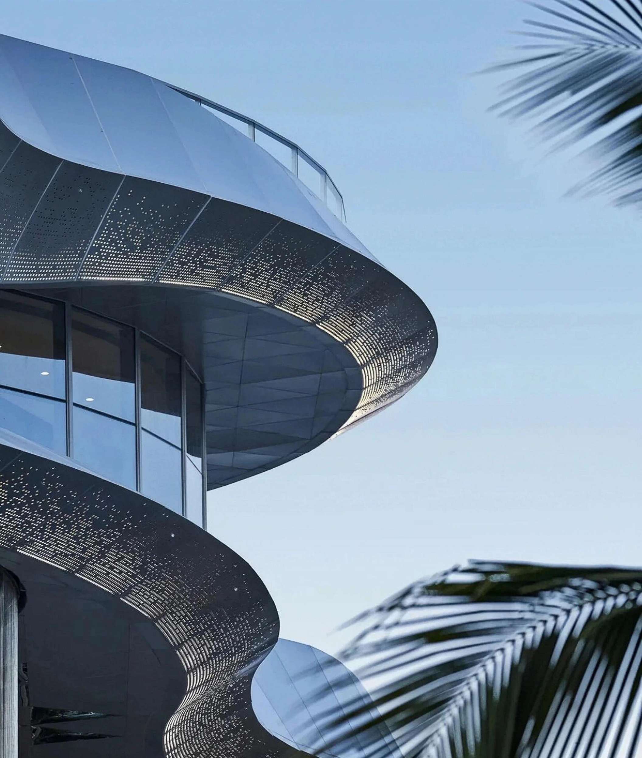 Curved architectural facade clad with perforated stainless steel panels that shift from open to dense