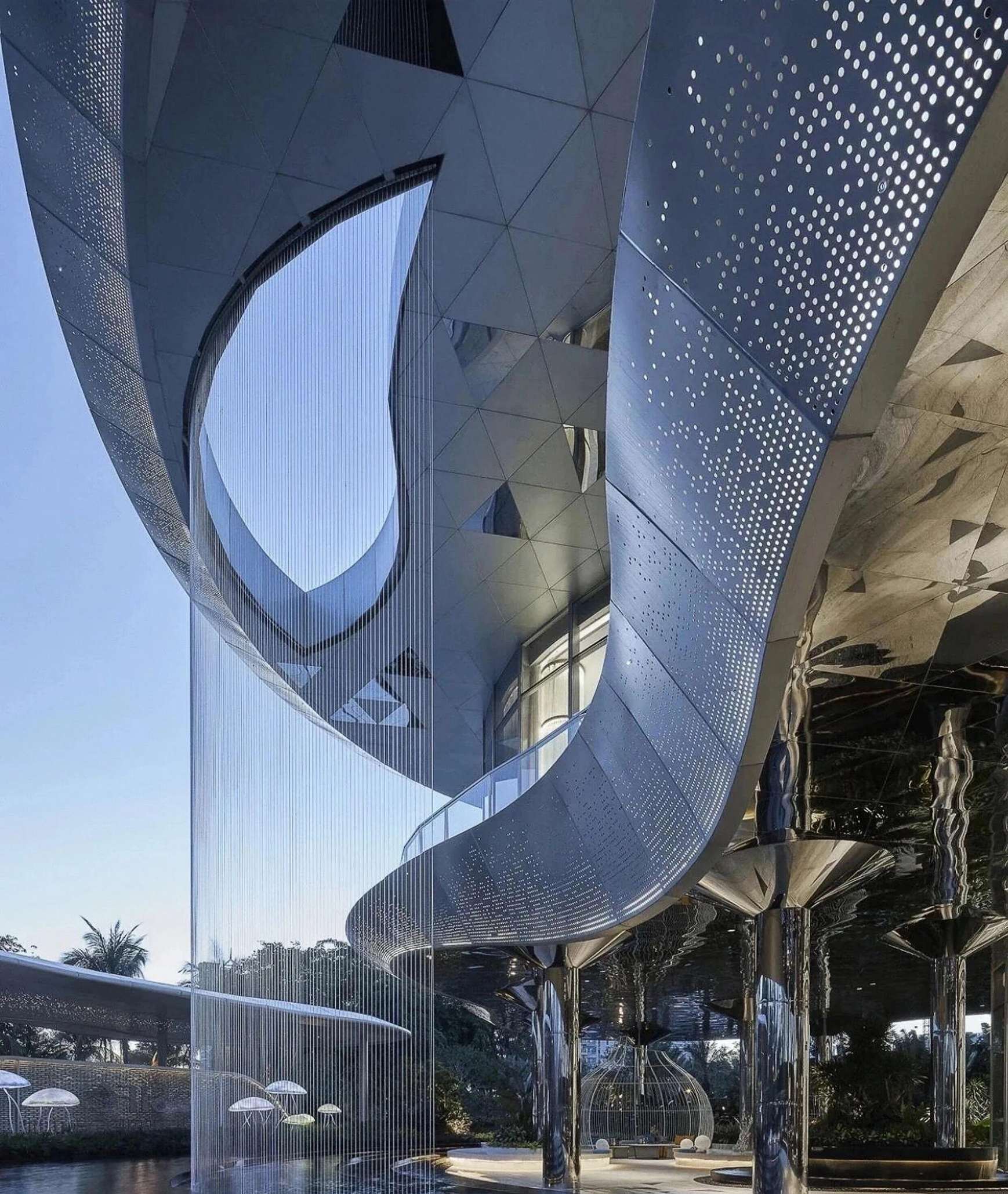 Curved perforated stainless steel canopy at a building entrance with mirror-finish columns