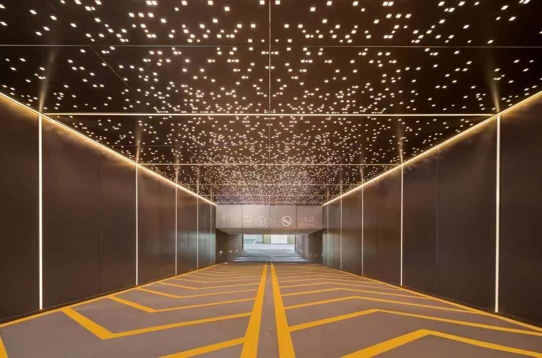 Perforated metal ceiling panels backlit at night, creating a starry light pattern