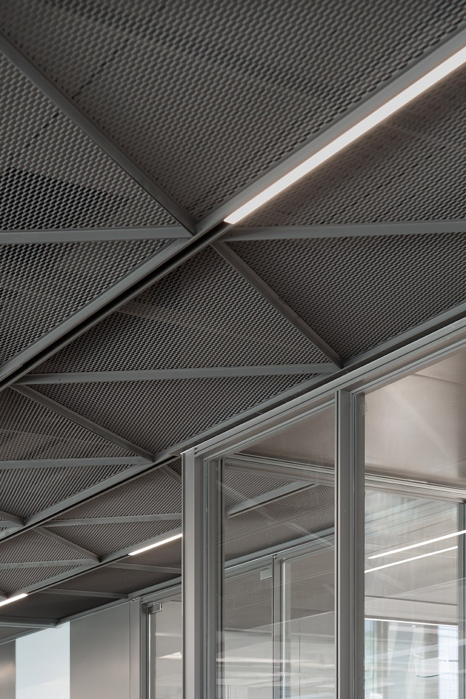 Perforated stainless steel lay-in ceiling panels on an exposed grid with a linear light runner