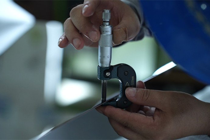 Caliper thickness measurement taken on a stainless steel sheet during inspection
