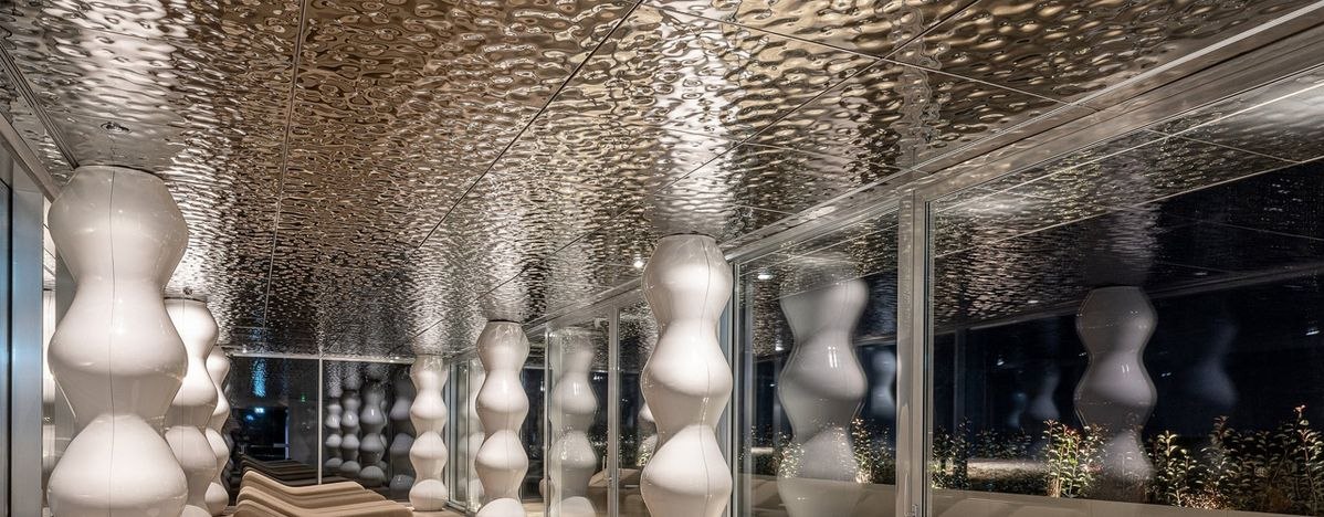 Lobby spanned by a water ripple mirror stainless steel ceiling reflecting soft daylight