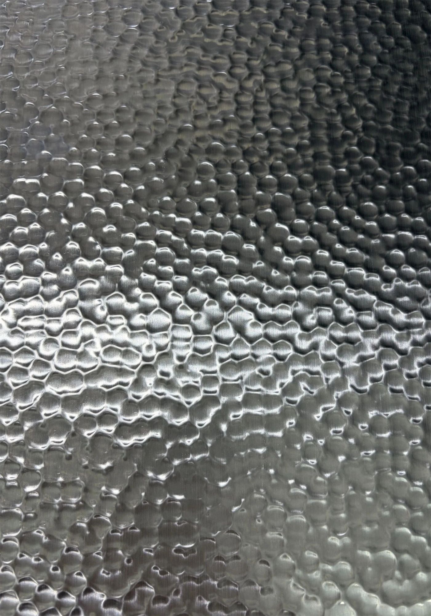 Macro of hammered stainless steel under raking light revealing peaks, valleys and depth