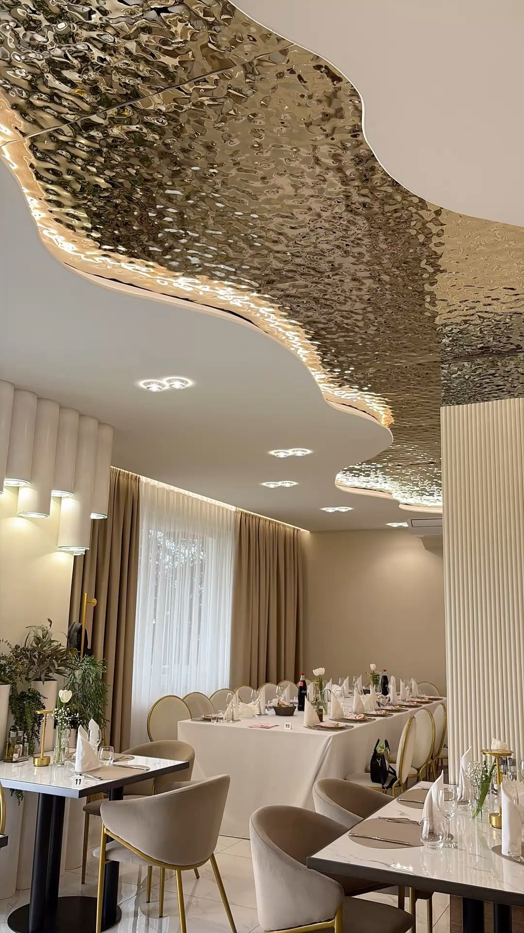 Gold water ripple stainless steel ceiling forming a reflective cloud over a dining room