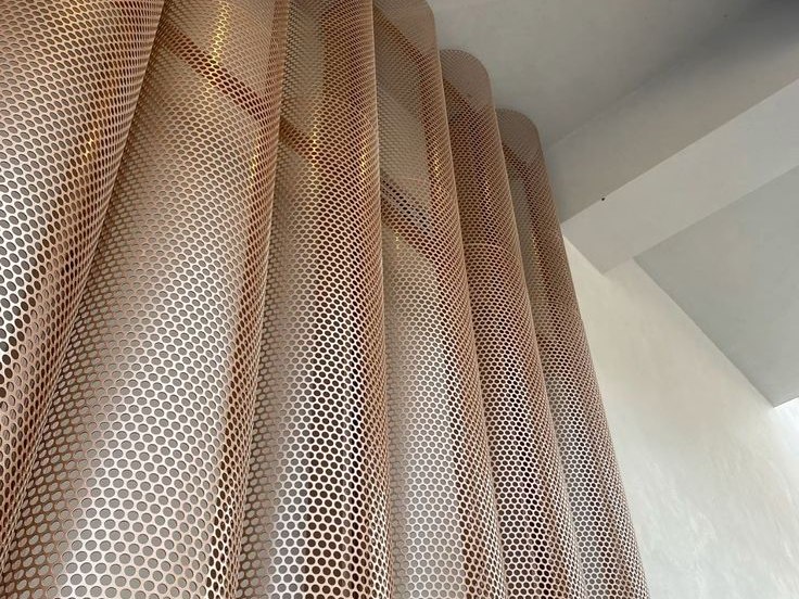 Rose gold perforated stainless steel partition screen dividing an interior