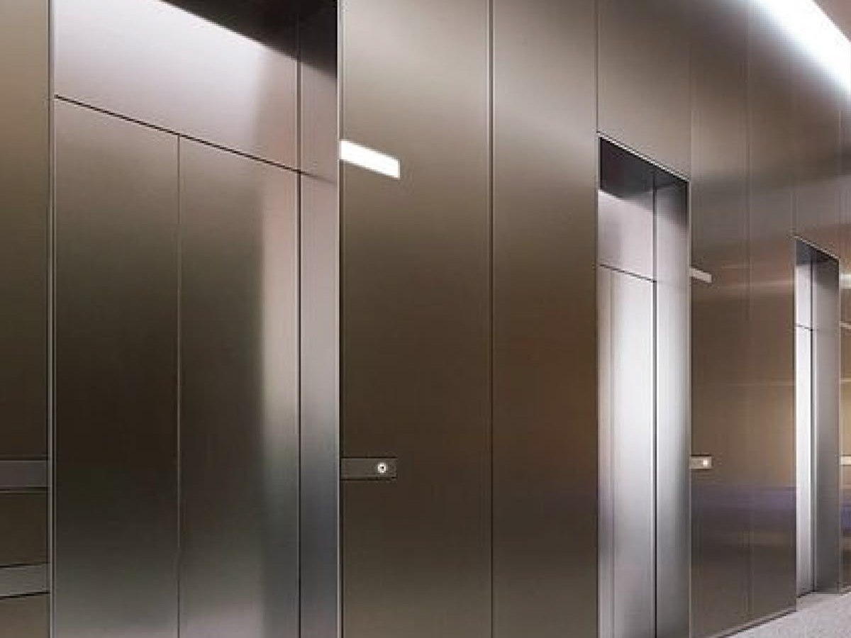 An elevator cabin interior clad in brushed stainless steel where surfaces are touched repeatedly
