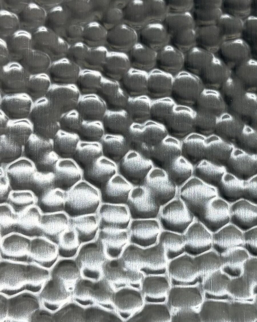 A hammered stainless steel surface where raised areas catch light and recesses fall into shadow