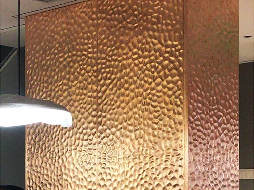 A reception counter clad in hammered stainless steel with a honed stone top