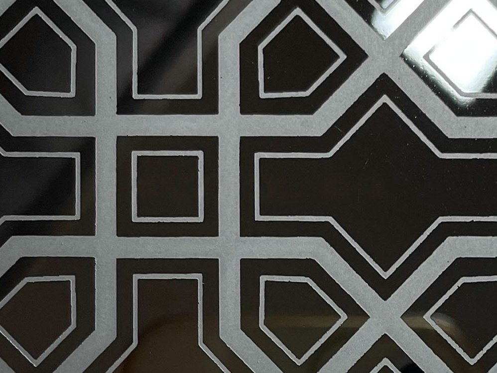 Etched stainless steel with strong contrast between treated and untreated areas making the geometry read clearly
